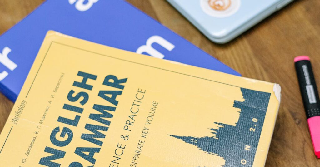 High-angle view of an English grammar book and a laptop with stickers on a wooden desk.